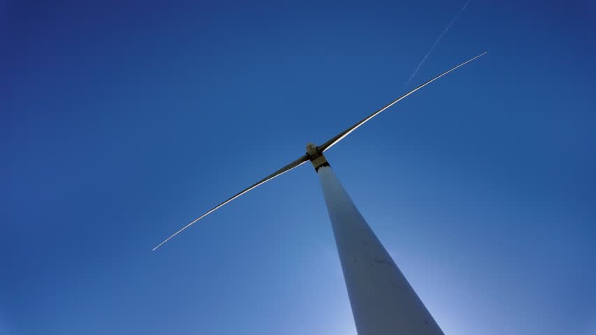 Low angle slow motion shot looking up a turbine tower into blue sky