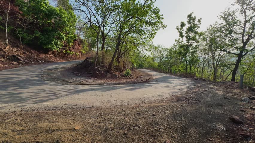 Tracking shot showcasing a dramatic hairpin curve on a winding mountain road surrounded by woodland vegetation highlighting scenic travel routes through rugged hilly terrain