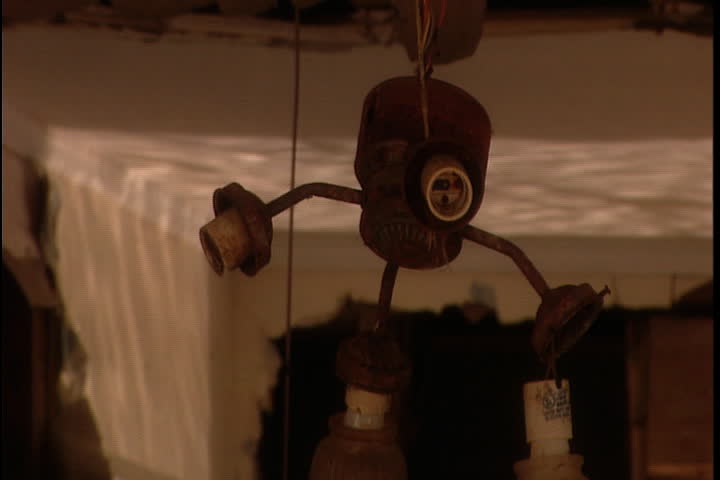 Broken light fixture dangling down into wrecked kitchen, water is reflected on toppled refrigerator in the background in New Orleans after Hurricane Katrina.