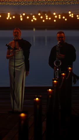 Female singer and saxophonist performing on a candlelit wooden stage at dusk