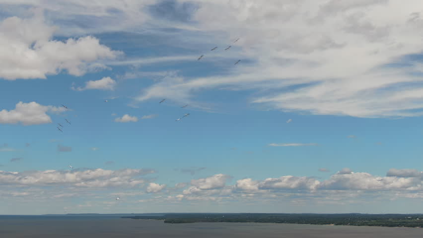 A wide static aerial shot of the Green Bay coastline featuring a vast blue sky with wispy white clouds and birds flying over the water.