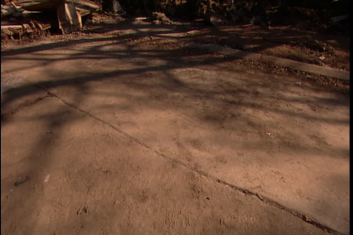 Cracked ground covered in silt, camera swings up to show damaged houses in neighborhood near 17th Avenue levee break in New Orleans after Hurricane Katrina.