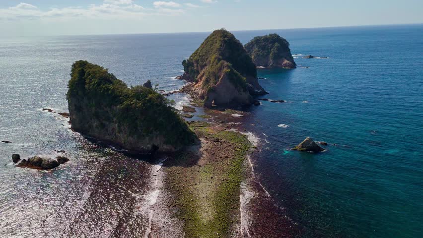 Drone shot moving back over a rocky tombolo land bridge exposed at low tide, leading toward the beautiful Sanshiro Islands in Izu.