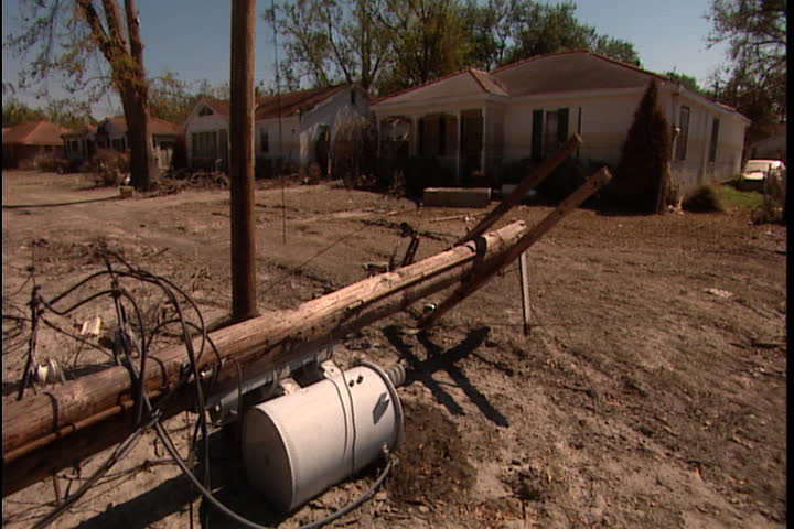 Fallen telephone pole on silt covered ground, houses in background in New Orleans after Hurricane Katrina.