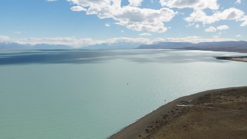 Lago Argentino near El Calafate, Santa Cruz, Argentina, featuring glacial waters, remote shoreline and Patagonian mountains beneath bright skies, drone descending aerial shot.