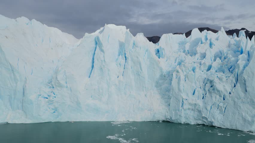 Perito Moreno Glacier in Los Glaciares National Park, Santa Cruz, Argentina, revealing seracs, crevasses and fractured ice structures beneath Andean peaks, telephoto orbit drone shot.