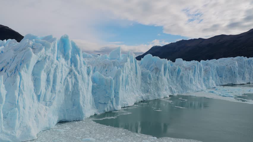 Perito Moreno Glacier in Los Glaciares National Park, Santa Cruz, Argentina, featuring towering blue ice formations above Lago Argentino, drone forward oblique flyover shot.