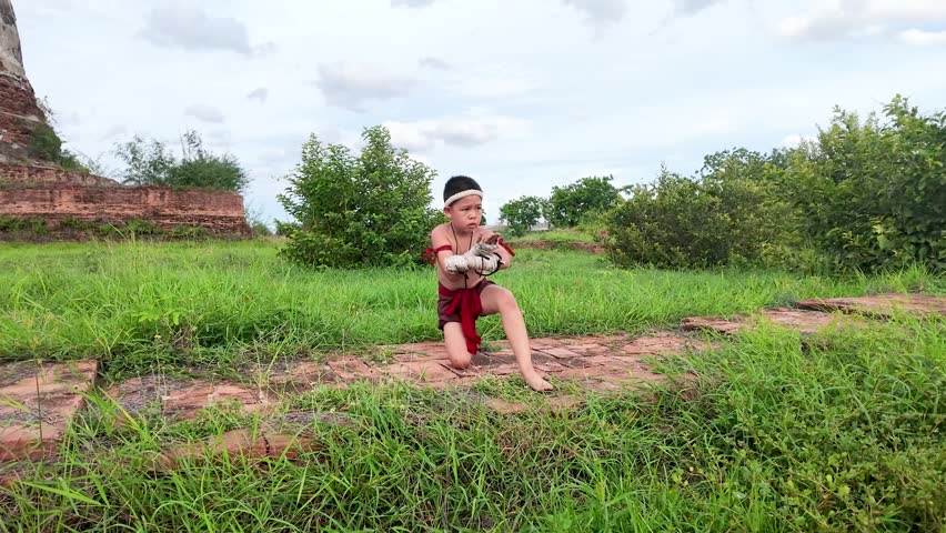 Asian child in traditional costume practices martial arts movements outdoors at a historical temple site.
