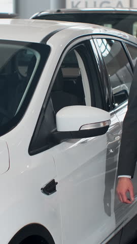 Vertical Video Man is choosing new automobile walking around luxury car and touching it in car dealership. Rich people, transportation and business class vehicles concept.