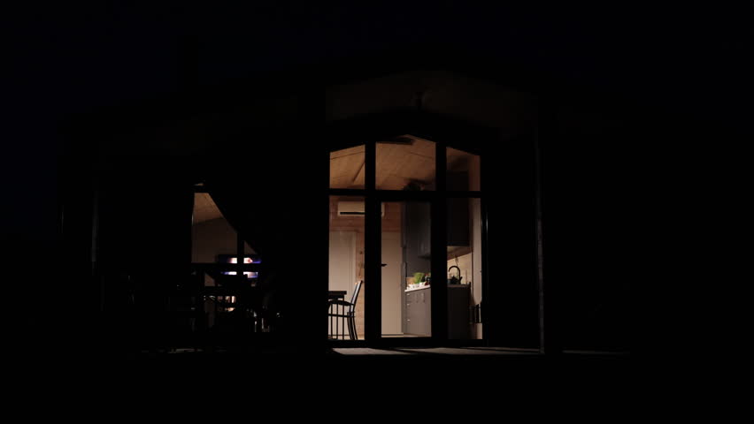 A young woman stands in a brightly lit kitchen at night, illuminated by interior lights while working on a counter