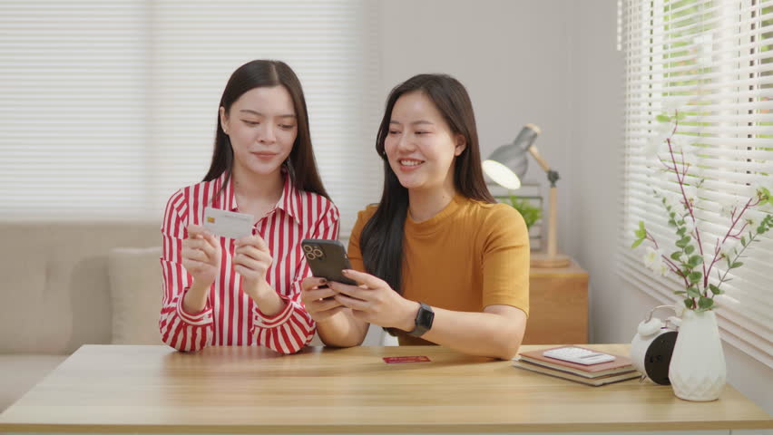 Two women using a credit card for online payment on a smartphone, ideal for e-commerce, mobile banking, digital transaction, online shopping and cashless payment concepts.