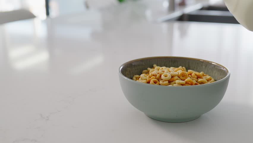 Close-up of milk being poured into a bowl of breakfast cereal. Splashing milk and crunchy cereal create a fresh morning breakfast scene in a home kitchen.