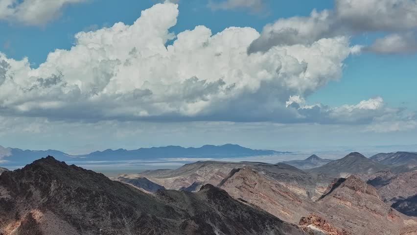 Clouds cover the sky above a rugged mountain range in the USA. The landscape stretches far into the distance, showing valleys and distant peaks under a blue sky.