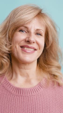 Cheerful beautiful mature woman with blonde hair smiling and looking at the camera. Her hair flutters in the wind in a studio