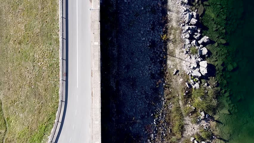 Top-down aerial footage of the shoreline and road at Lake Zaovine in Tara National Park, western Serbia. Clear green water, rocky coast and scenic landscape.