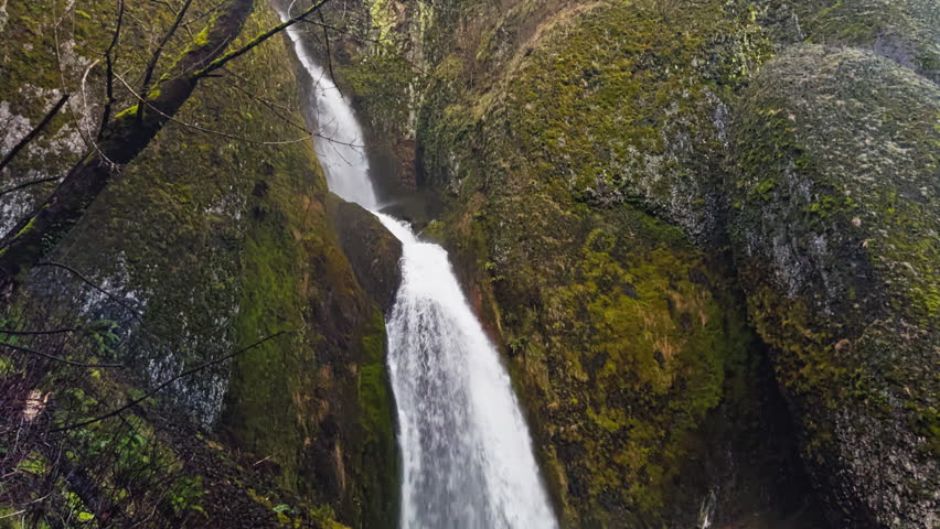 Wahkeena Falls cascading through a narrow moss lined basalt canyon, tilt down passing old fern covered bridge walkway