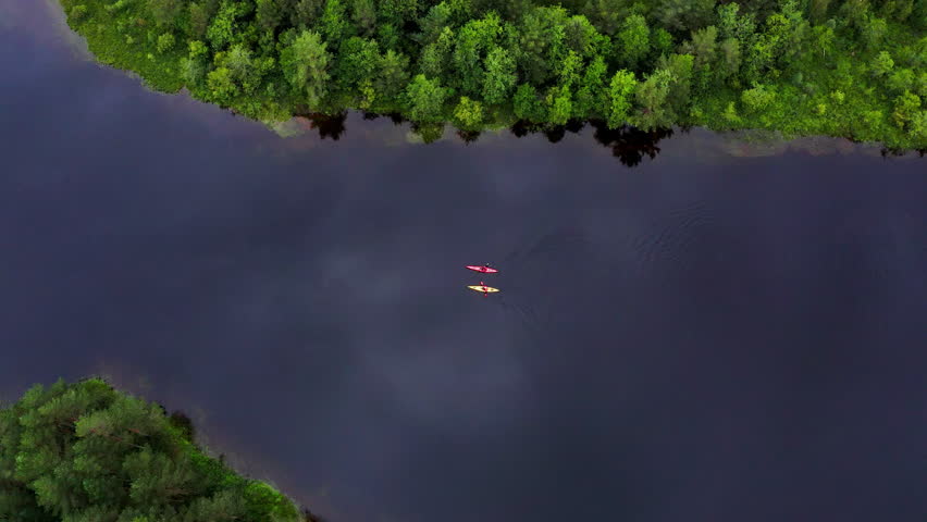 Top aerial view of yellow and red kayaks with two people paddling on scenic mountain lake surrounded by pine tree forest in Norway, active summer outdoor travel