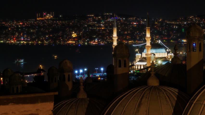 A breathtaking night view of the Istanbul skyline featuring an illuminated mosque with minarets overlooking the dark Bosphorus sea and glowing city lights across the hills