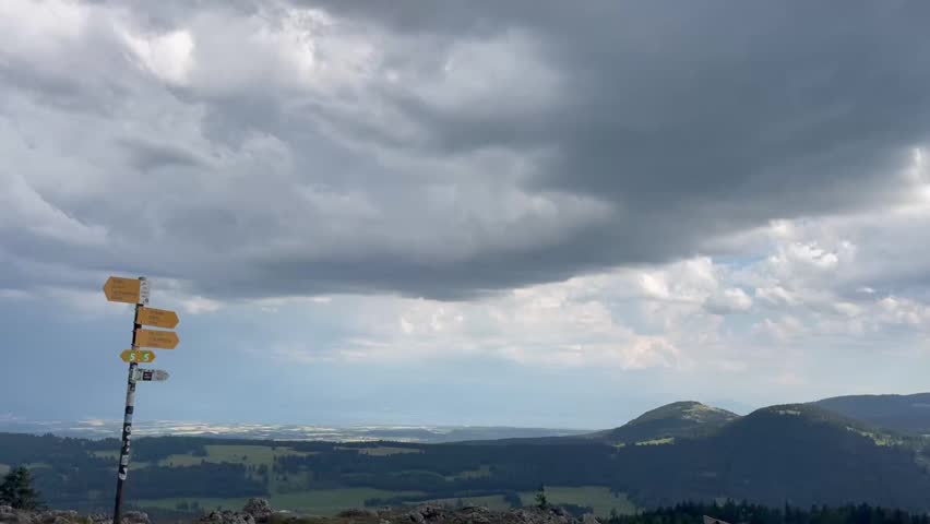 Panoramic view from a mountain top overlooking a valley, lake, and beautiful cloud formations.