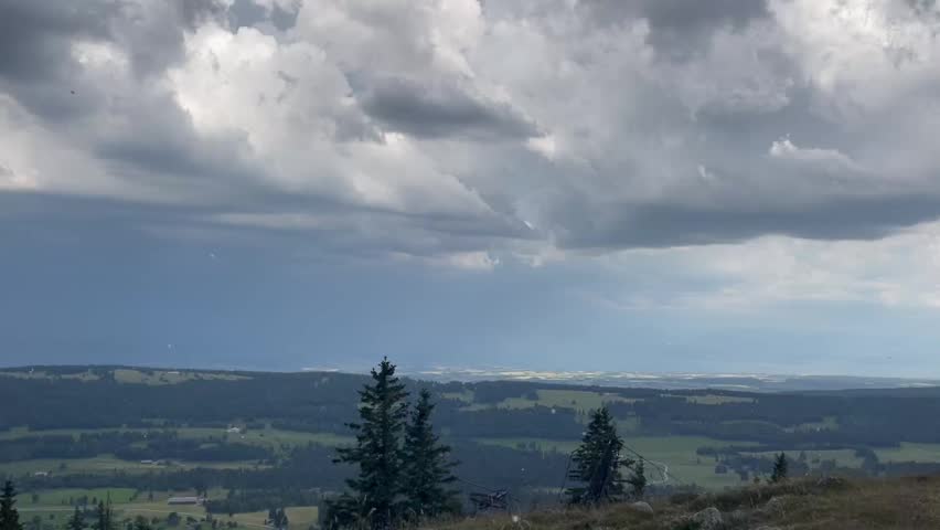 Panoramic view from a mountain top overlooking a valley, lake, and beautiful cloud formations.