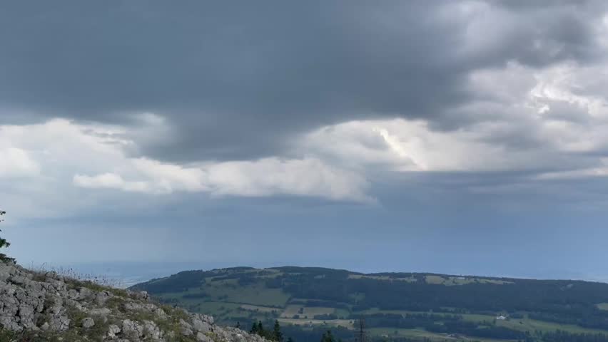 Panoramic view from a mountain top overlooking a valley, lake, and beautiful cloud formations.