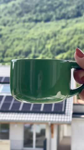 Morning in the mountains with a green tea mug, summer flowers, and an eco-friendly house.