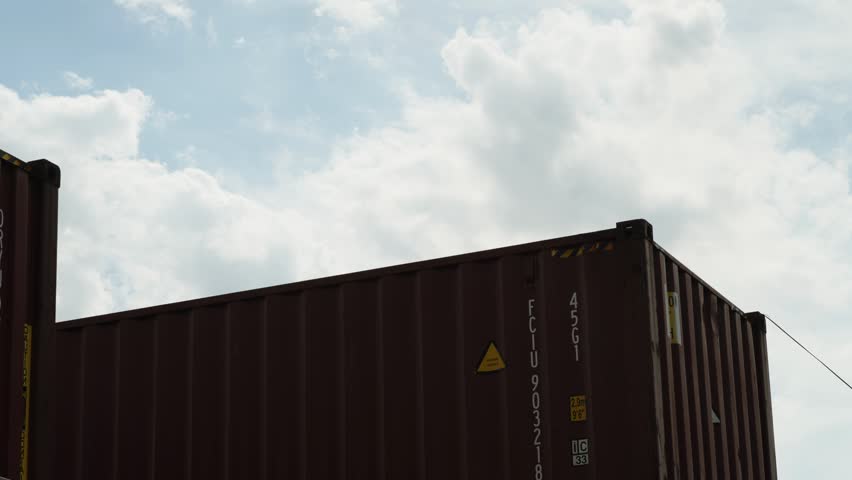  Large brown shipping containers standing under a cloudy blue sky
