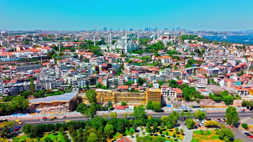 Aerial view of Istanbul, Turkey near the Blue Mosque. The Sultan Ahmed Mosque stands within a sunny historic cityscape of red rooftops, roads and distant sea.