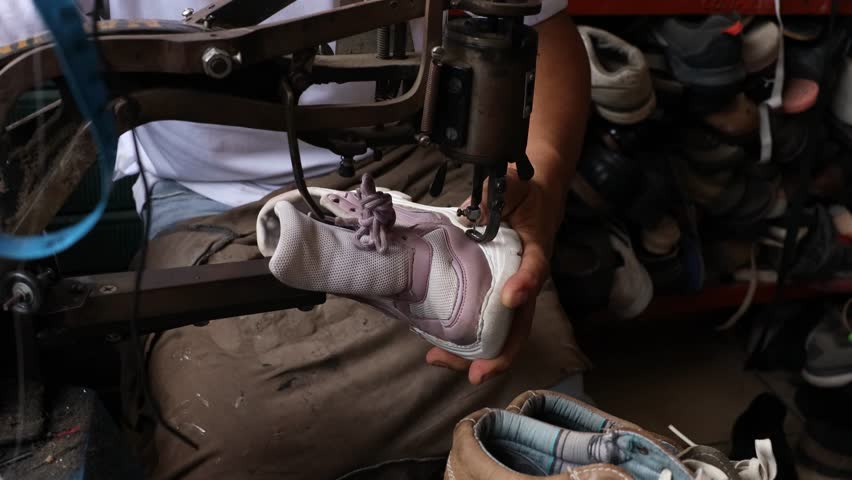 Male cobbler hands sewing a sneaker sole using an old industrial machine in his workshop