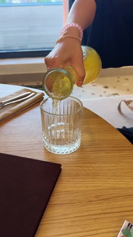 Pouring ginger-pineapple lemonade from a pitcher into a glass, set against a summer landscape visible through the window.