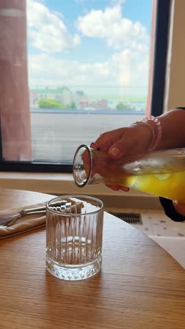 Pouring ginger-pineapple lemonade from a pitcher into a glass, set against a summer landscape visible through the window