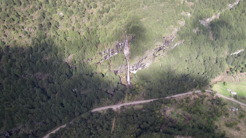 Aerial view of a waterfall cascading down a steep forested mountain cliff