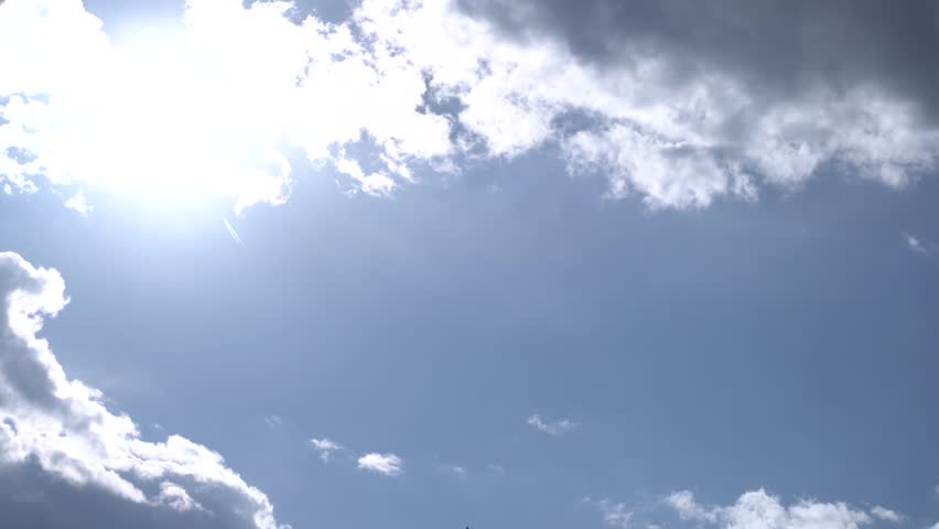 Sunrays behind white clouds in morning sky.