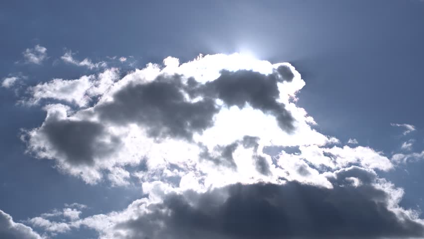 Sunrays behind white clouds in morning sky.