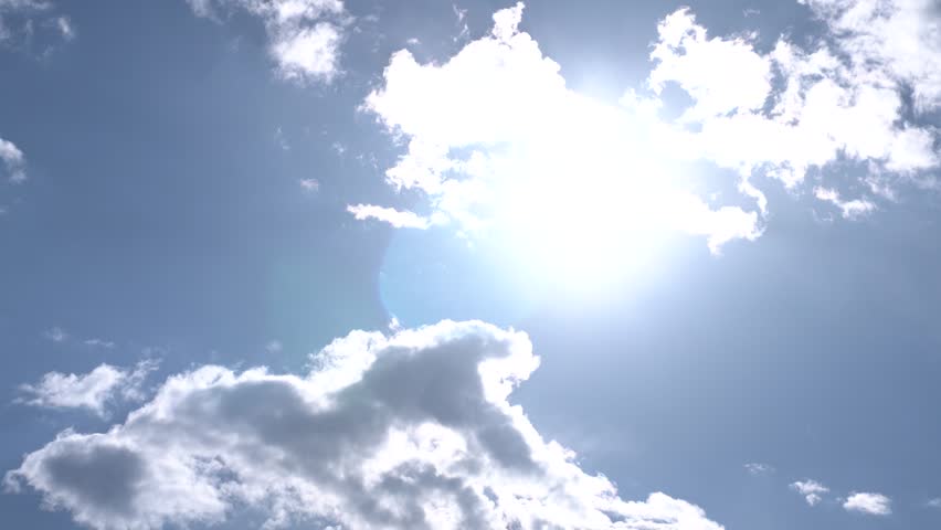 Sunrays behind white clouds in morning sky.