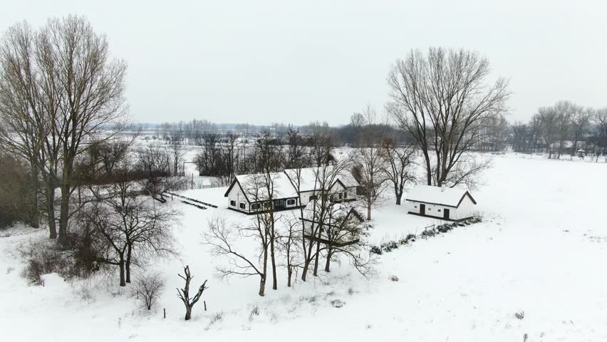 Bugac, Hungary a drone flying above a farmhouse covered with snow during an overcast winter day