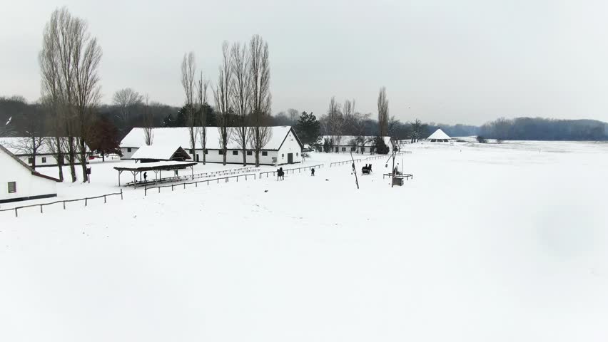 Flock of birds flying over a snowy traditional hungarian farm in Bugac, Hungary and people riding horses