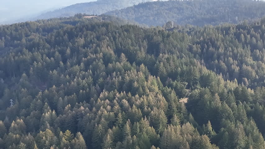 Aerial panoramic view of rolling mountain ridges and hazy valley under a bright cloudy sky in California