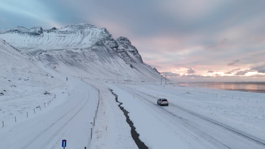 Drone view of car driving by snowy mountain in winter Iceland