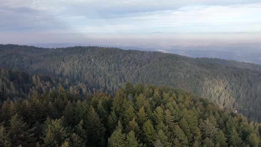 Aerial panoramic view of rolling mountain ridges and hazy valley under a bright cloudy sky in California