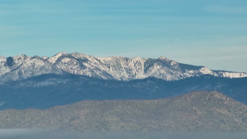 Aerial view of forested mountains with patches of winter snow under a cloudy sky in California