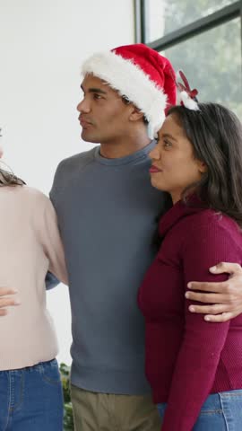 Vertical video: Offframe voice calling man in Santa-hat, woman in sweater leaning, posing by window. Holiday, family, friends, reindeer, antlers, festive, vertical video