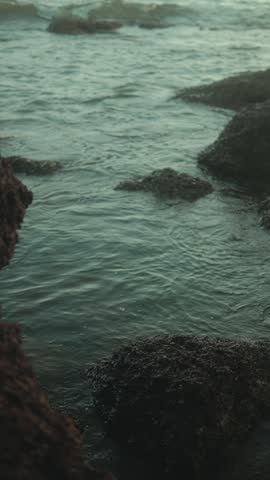 Waves gently washing over dark rocks in a coastal tide pool at the shoreline