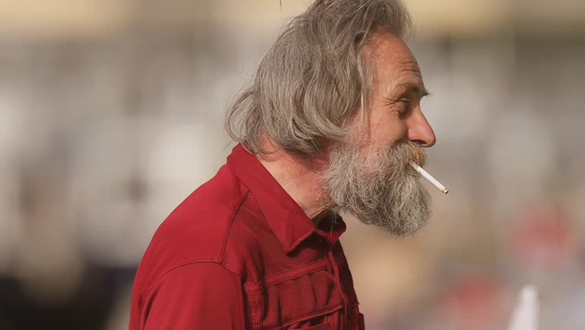 Elderly homeless man searching for something in garbage bin and on city street