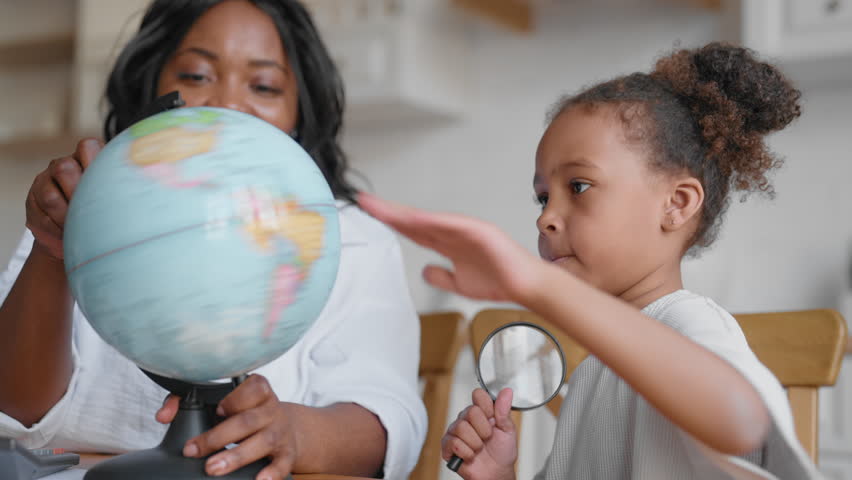 African american mom teaching her daughter at home, showing globe to girl. Geography lesson in school. Preschooler child enjoy fun geography lesson, education and homeschooling, exploring world