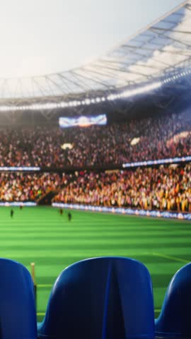Vertical video: Stadium tribunes fill foreground with blurred pitch and players behind, showing live match action in a sports arena.