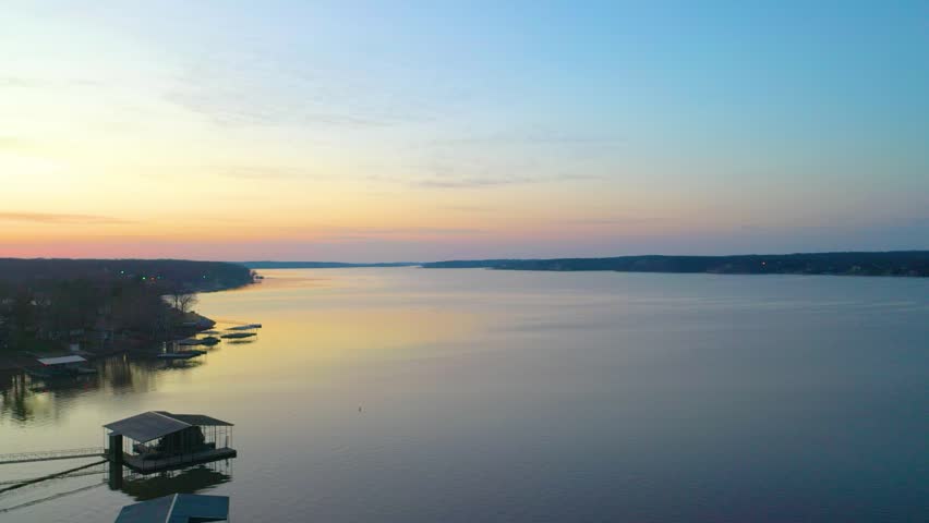Scenic Beaver Lake aerial landscape with calm reservoir water, forested Ozark shoreline, lakeside homes, covered docks, and colorful evening sky for travel or vacation footage.
