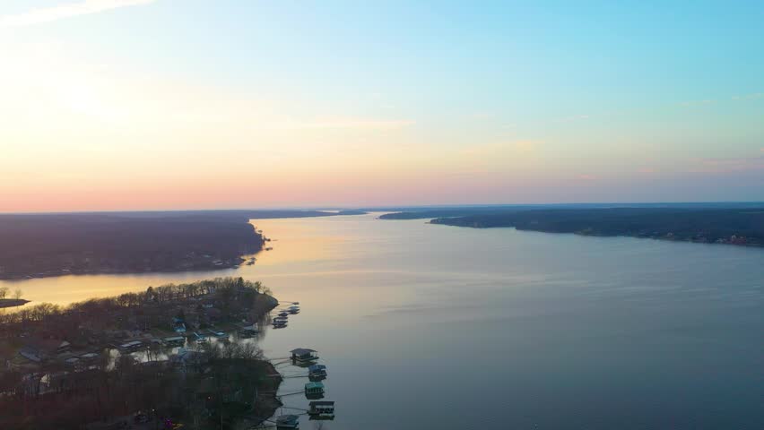 Peaceful Lake Cumberland drone view with waterfront homes, covered boat docks, forested coves, calm evening water, and warm sunset glow across the scenic Kentucky lake landscape.
