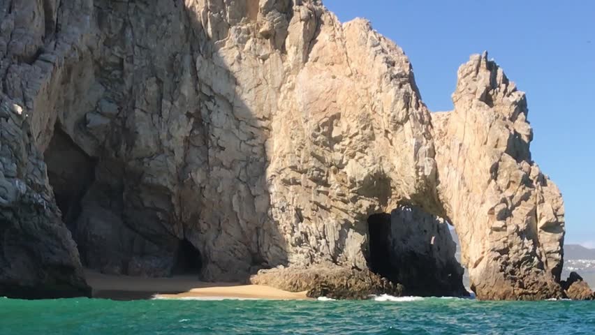 Coastal view of towering granite sea cliffs, rock formations and a secluded sandy beach beside turquoise waters along the shoreline of Cabo San Lucas, Mexico