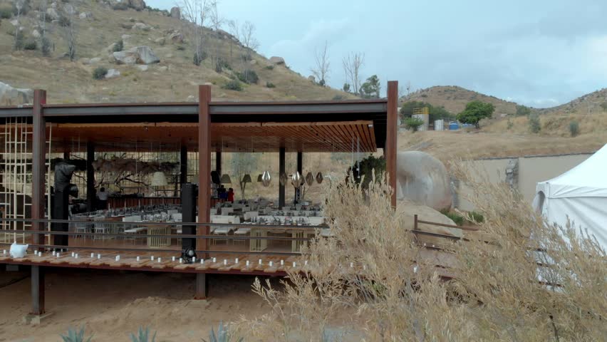 Drone view of an open air restaurant with dining areas and pavilion structures, set within an arid hillside landscape in Mexico.